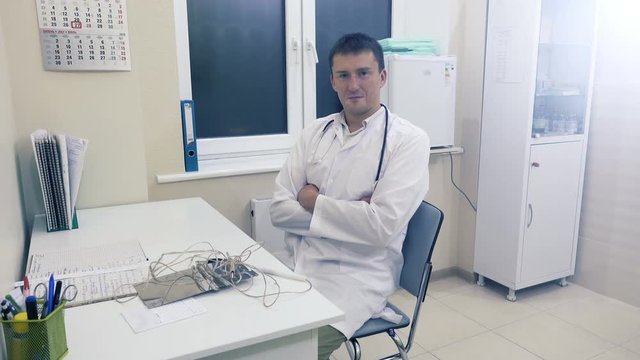 Young doctor with stethoscope sits on a chair in his office