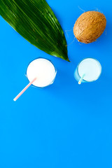 Light cocktail with coconut milk. White tropical beverage in glasses with straw on blue background with coconut and palm leaves top view copy space