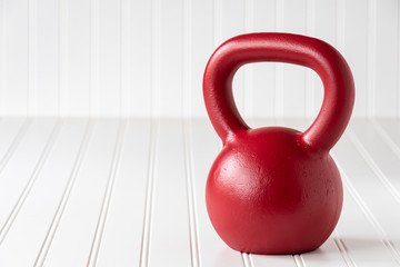 Red kettle bell on a white bead board background
