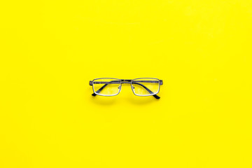 One glasses with transparent lenses on yellow background top view copy space