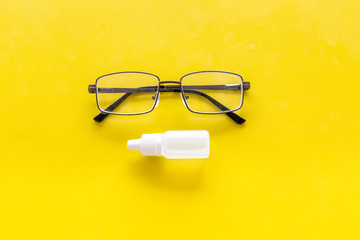 Eye drops in small bottle near glasses on yellow background top view copy space