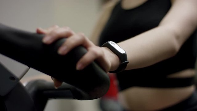 cute girl in black sport wear hardly work on exercise bike with focus on hands in the new gym