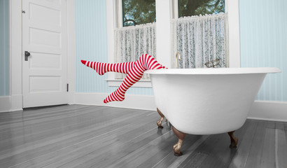 Legs in red and white striped tights hanging over edge of antique bath tub in blue, vintage bathroom