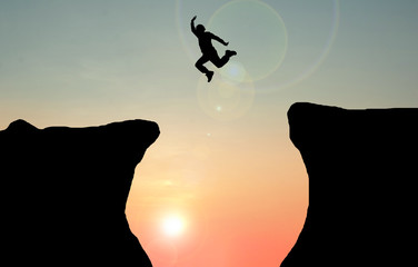 Silhouette  concept idea. A man jumping over cliff on sunset background. A  man jumping between the rock mountains. Freedom , active 