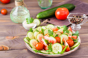 Vegetable salad of fresh cucumbers, tomatoes, parsley and sesame seeds on a plate on a wooden table. Ingredients for salad preparation