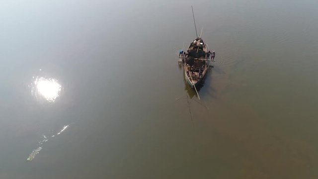 Aerial view. Manual extraction of sand and clay for construction of Indian workers with the help of long poles, buckets and ropes, standing on a small wooden boat in the middle of the river. 