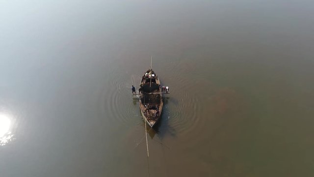 Manual extraction of sand and clay for construction of Indian workers with the help of long poles, buckets and ropes, standing on a small wooden boat in the middle of the river. Shooting with a drone.