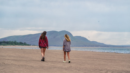 Two girls walk along the sandy beach against the mountains