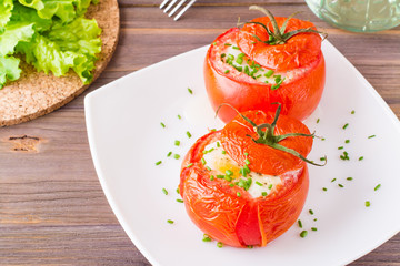 Fresh tomatoes baked with cheese and egg sprinkled with green onions on a plate on a wooden table