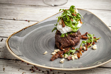 a large piece of juicy steak with egg poached and rucola salad with goat cheese in olive oil, lies...