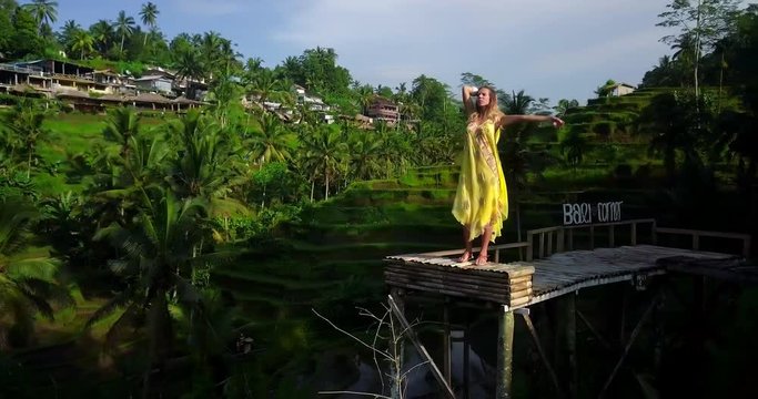 Young lady in yellow fashion dress. Girl explore world. Typical Asian hillside with rice farming. mountain shape green cascade rice field terraces paddies. Ubud. Bali. Indonesia. Aerial drone view.