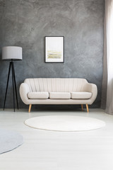 Poster on a gray wall, above a beige, leather sofa and a tripod floor lamp in a modern living room interior