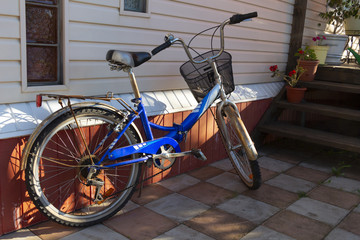 A blue bicycle stands in the courtyard of a private house near the porch.