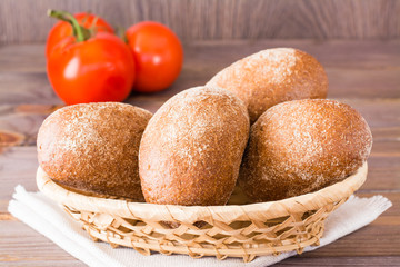 Fresh rye buns in a basket and tomato on a wooden table