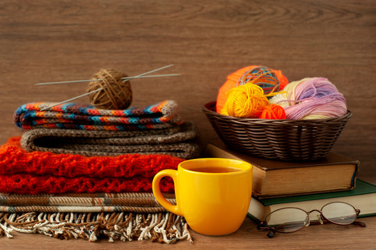 Knitting and cozy atmosphere. Colorful yarn in a basket, a cup of tea, knitted clothes, plaid and sunglasses create coziness in the house. Needlework in the form of knitting.