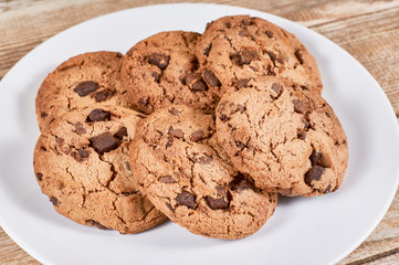 oatmeal cookies with chocolate slices in a white plate on a wooden background, close-up