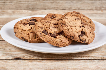 oatmeal cookies with chocolate slices in a white plate on a wooden background, close-up