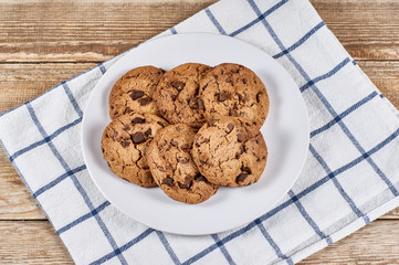 oatmeal cookies with chocolate slices in white plate and napkin on a wooden background