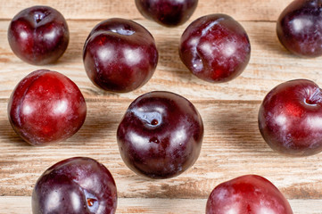 several plums are scatter on wooden background, close-up