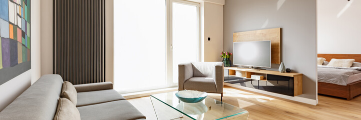 Television on wooden cabinet in living room interior with armchair next to window. Real photo