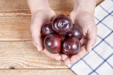 female hands holds few red plums next to a doily with figure on a wooden background