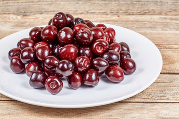 cherry in a white plate on a wooden background