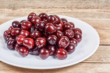 cherry in a white plate on a wooden background
