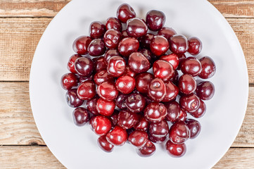 cherry in a white plate on a wooden background, flat lay