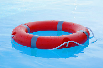 Red lifebuoy pool ring float on blue water. Life ring floating on top of sunny blue water. Life...