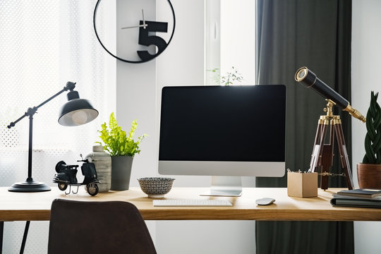 Close-up photo of mockup computer standing on wooden desk with vintage telescope, fresh green plants and metal lamp