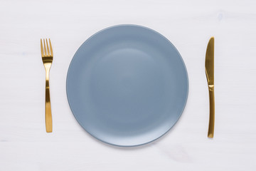 Table setting with an empty round plate, golden fork and knife.