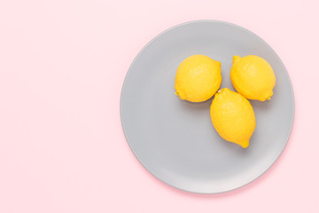 Three yellow lemons in the plate on pink background with negative space.