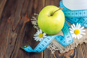 Bottle of kefir, green apple and tape measure on dark wooden background. Diet and slim concept.