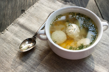 Soup with meatballs in a white bowl on the wooden background.
