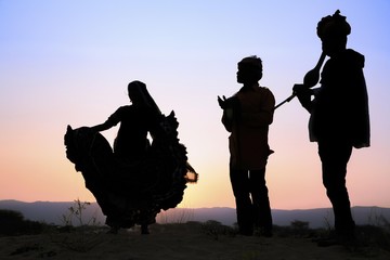 Woman dancing in front of setting sun with two musicians