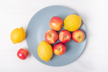 Fresh apples and lemons in a plate on white background.