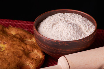 A bowl with flour and apricot cake on a wooden background