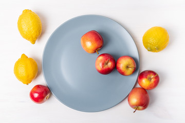 Fresh apples and lemons in a plate on white background.