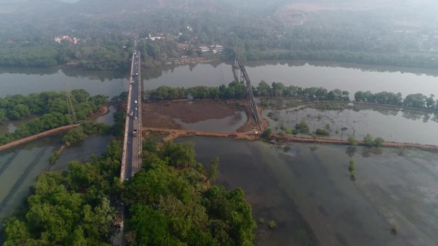 Flying over a large road bridge and aqueduct over the river in Goa, India. Aerial view at high altitude.