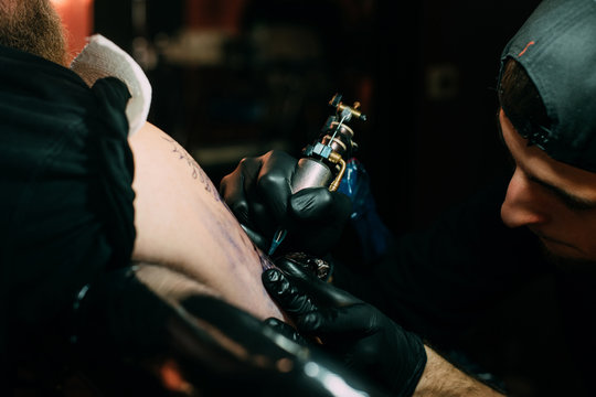 selective focus of tattoo artist in gloves with tattoo machine working on tattoo on shoulder in salon