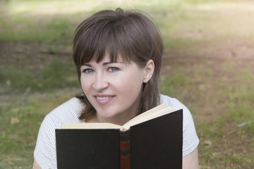 Lovely girl in the park reading a book and smiling close-up