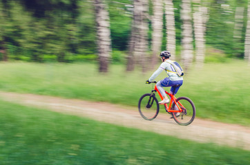 A cyclist in a helmet rides through the forest on a bicycle path, motion blur