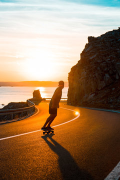 Young man skateboarding on empty street, sea sunset in background