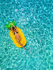 Junge, sportliche Frau entspannt auf einer aufblasbaren Ananas in einem Pool an einem heißen...
