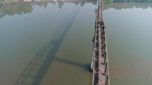 Aerial view. Flying over a long aqueduct over a muddy river. A shadow of the structure falls on the water of the river. Shot with a drone in Goa, India.