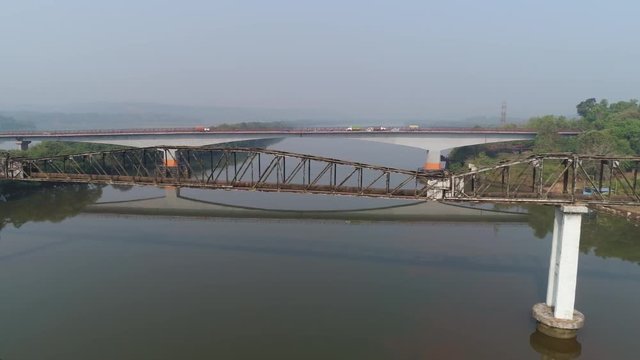 Aerial view. Flying along an old rusty aqueduct truss over the river. The cars are driving on a concrete bridge in the background. 