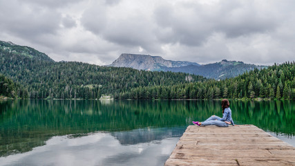 Girl sitting on the dock of the black lake in the Durmitor national Park. Montenegro.