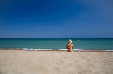 Fototapeta na wymiar A girl in a swimsuit and a hat sitting on the seashore in the sea.