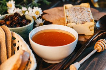 Honey in white ceramic bowl, honey dripper spoon, homemade honeycomb on rustic wooden table