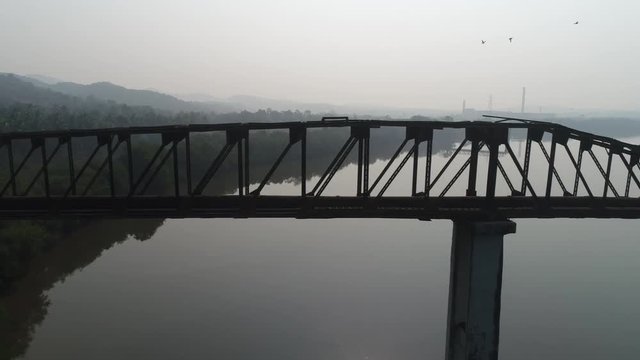 Aerial view. Silhouette of old, long, rusty truss-type aqueduct over the river. Shooting with a drone.